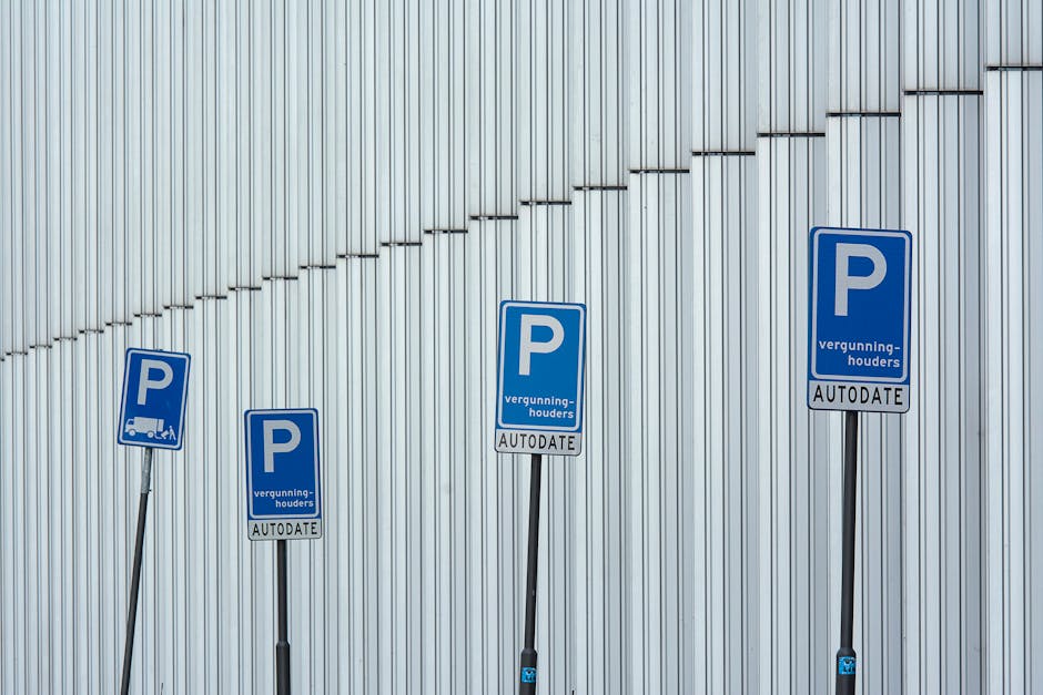 A blue and white parking permit sign indicating a designated accessible parking space, mounted on a metal pole positioned against a smooth, dark grey exterior wall. The sign displays a large white 'P'